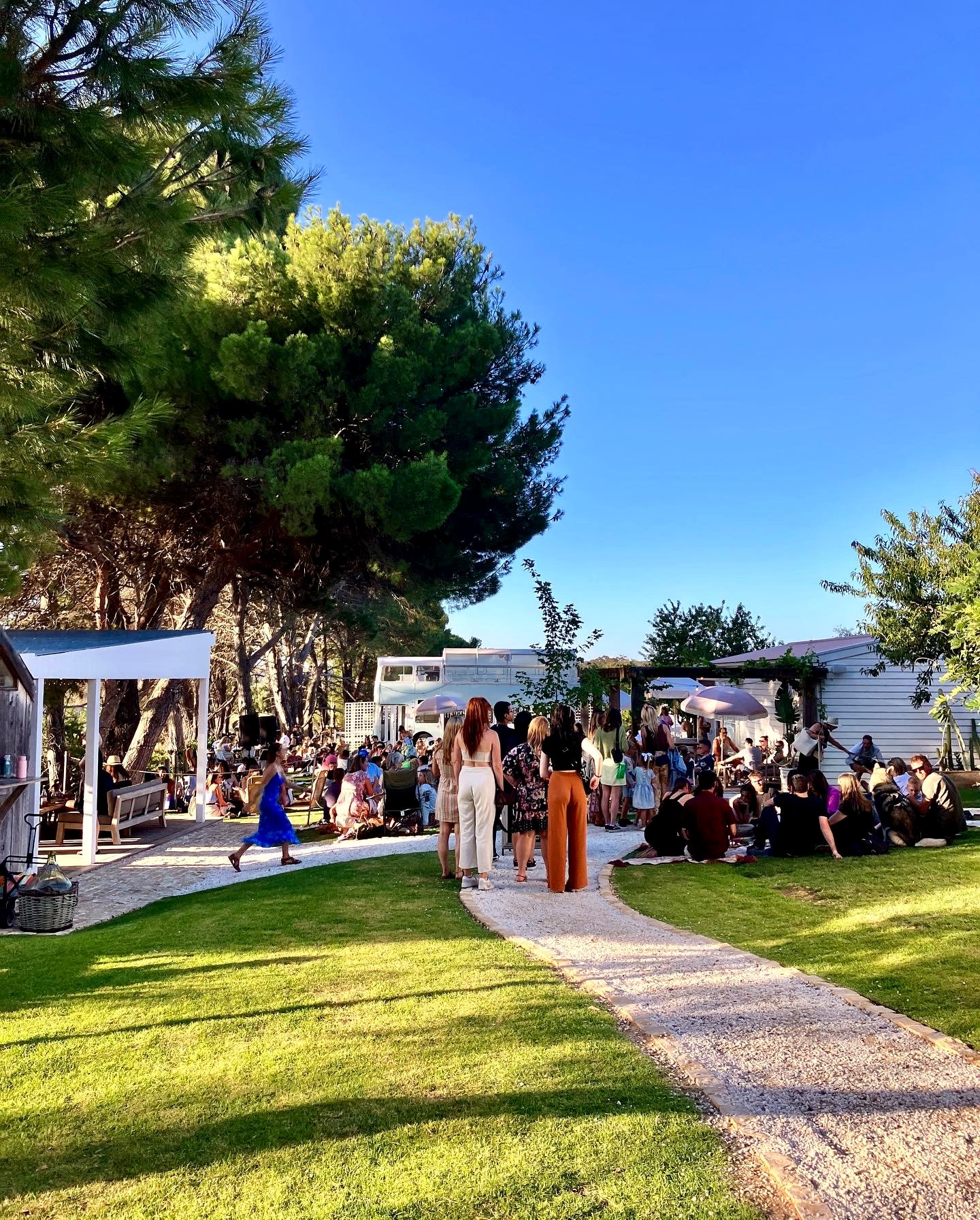 Scène extérieure de festival avec kiosques, public et ciel bleu.
