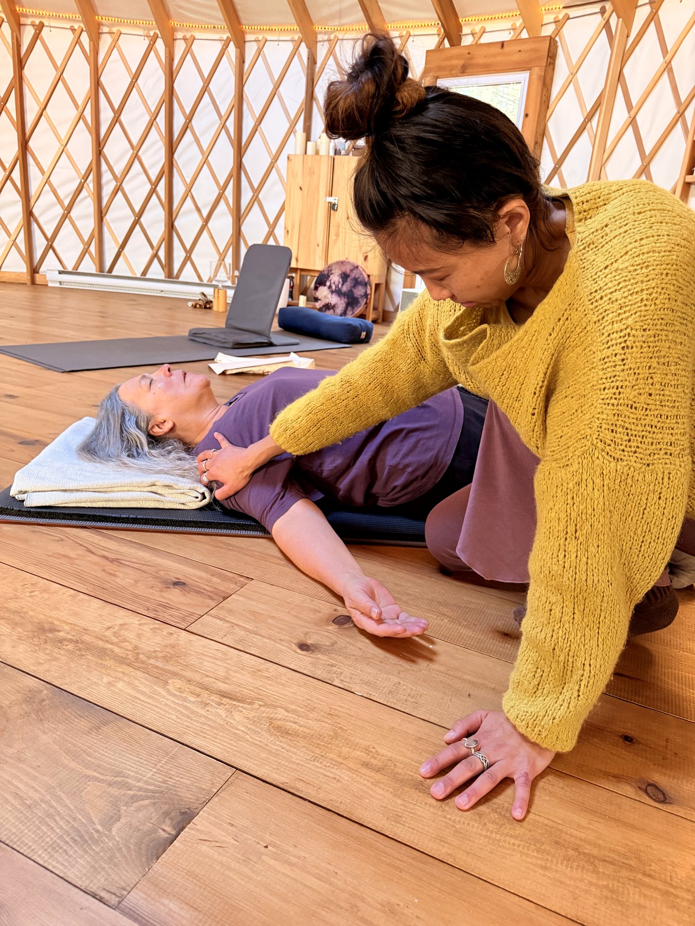 Letitia Rose soutient une personne allongée pendant une pratique douce sur tapis.